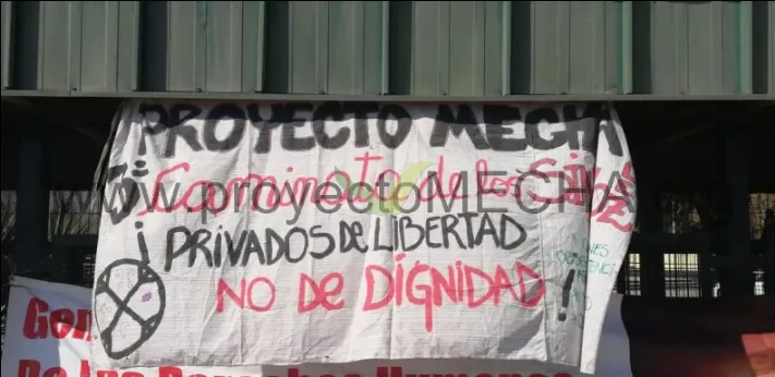 Pancarta blanca colgada en una marcha pública en Chile con el título PROYECTO MECHA escrito a mano y el lema '¡Privados de libertad, NO de dignidad!'; al costado, el símbolo de la A en círculo del activismo libertario